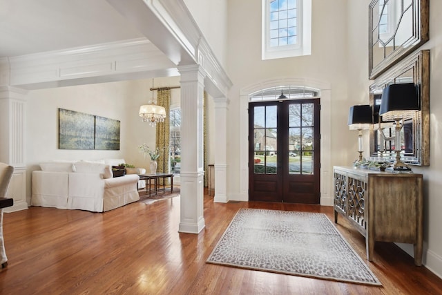 entrance foyer with ornate columns, a towering ceiling, a chandelier, hardwood / wood-style flooring, and french doors