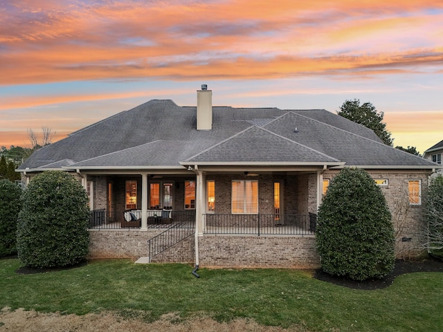 back house at dusk featuring a yard and a porch