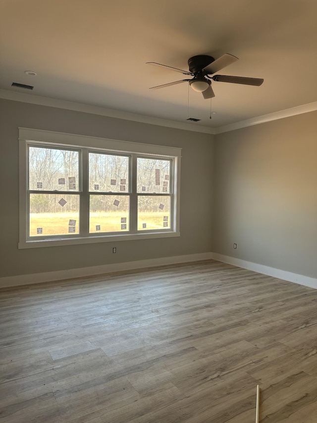 empty room featuring visible vents, crown molding, baseboards, and wood finished floors