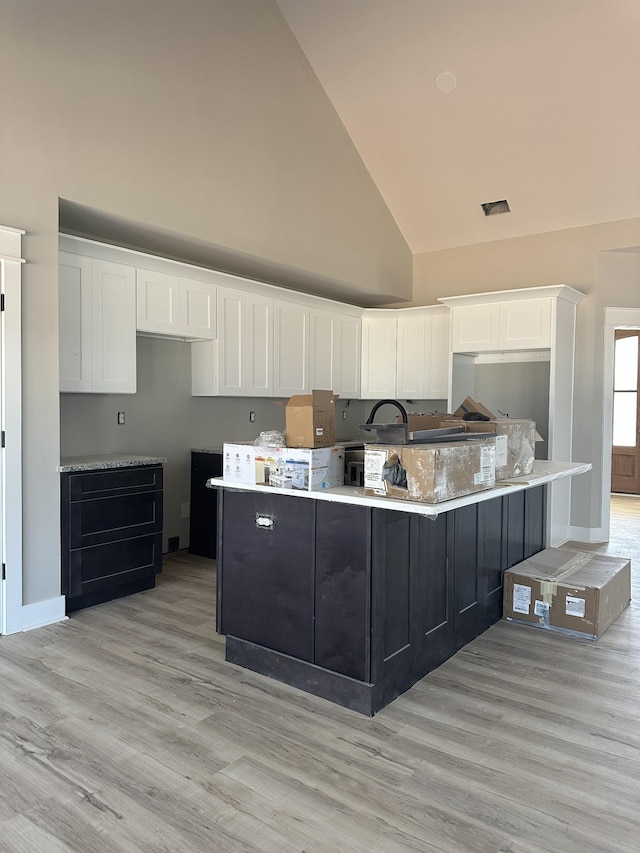 kitchen featuring light countertops, white cabinets, light wood-style flooring, and high vaulted ceiling