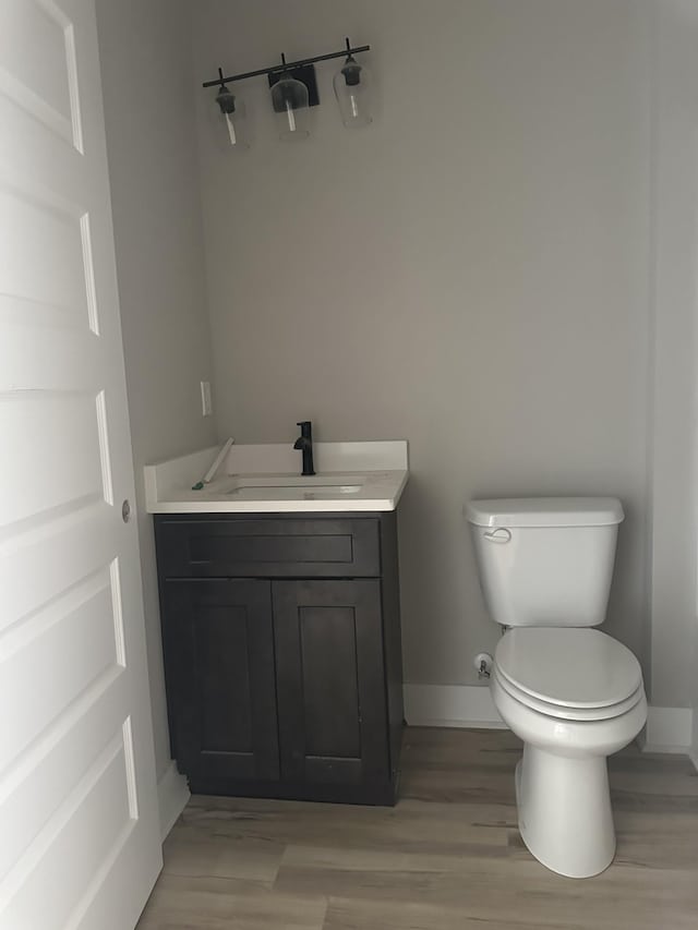 half bath featuring vanity, toilet, wood finished floors, and baseboards