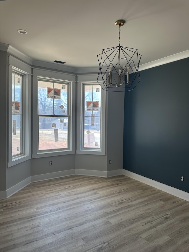 unfurnished dining area featuring visible vents, ornamental molding, wood finished floors, an inviting chandelier, and baseboards