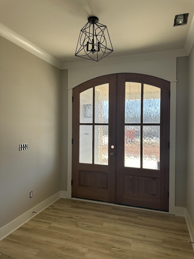 foyer with light wood finished floors, french doors, baseboards, and ornamental molding