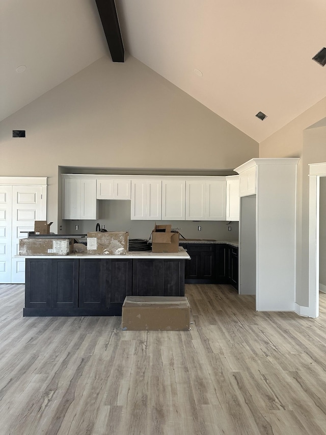 kitchen featuring beam ceiling, visible vents, white cabinets, and light wood-style flooring