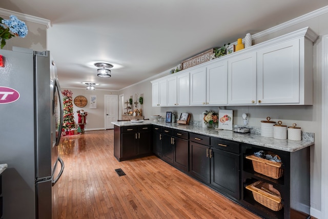 kitchen featuring white cabinets, light stone countertops, ornamental molding, light hardwood / wood-style floors, and stainless steel refrigerator