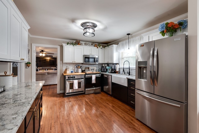 kitchen featuring white cabinetry, sink, stainless steel appliances, pendant lighting, and light wood-type flooring