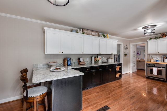 kitchen with crown molding, stainless steel oven, white cabinets, and light hardwood / wood-style floors