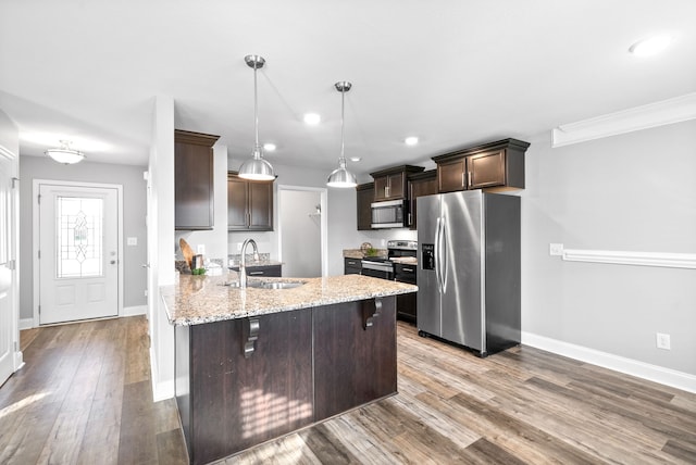 kitchen featuring sink, stainless steel appliances, light stone counters, decorative light fixtures, and light wood-type flooring