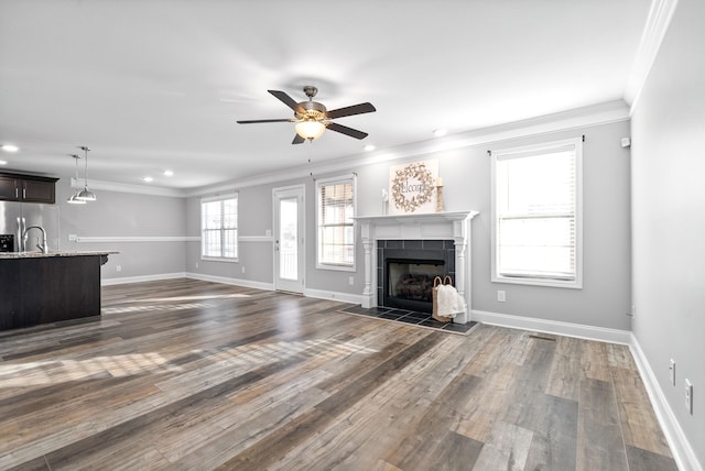 unfurnished living room featuring ceiling fan, crown molding, dark wood-type flooring, and a tiled fireplace