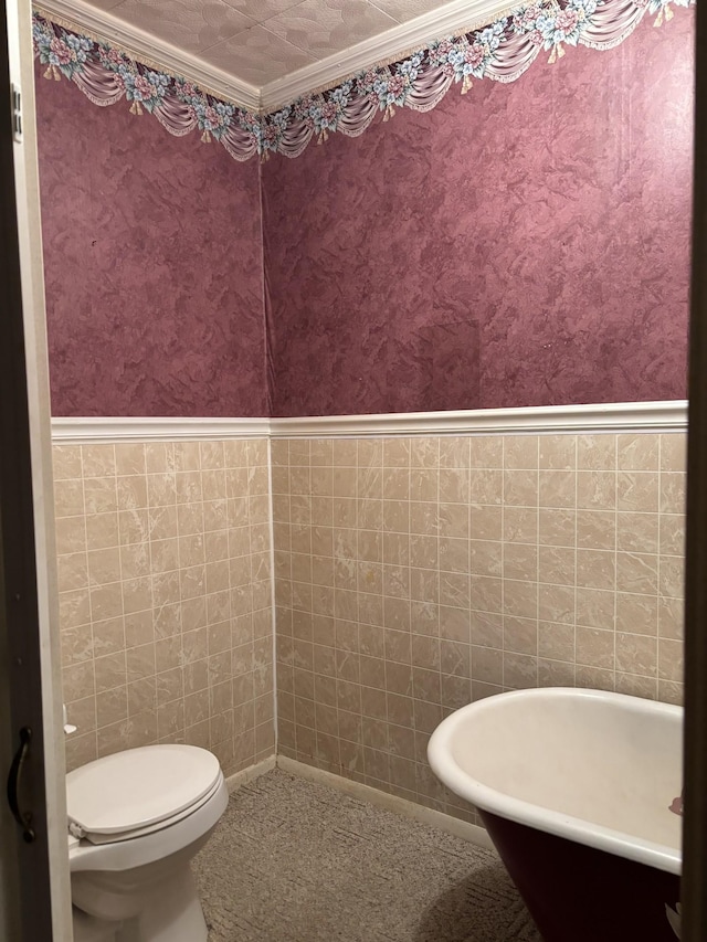 bathroom with a bath, toilet, tile walls, and crown molding