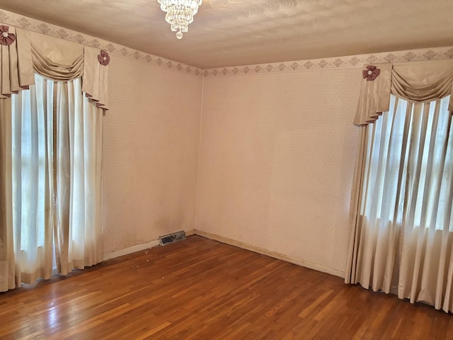 spare room with plenty of natural light, an inviting chandelier, and hardwood / wood-style flooring