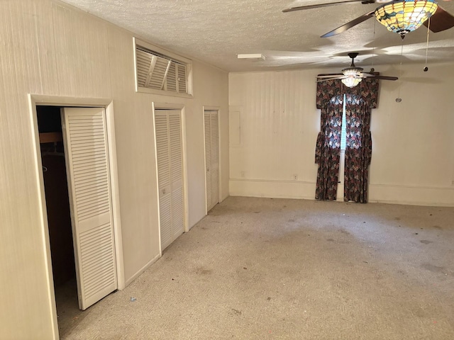 unfurnished bedroom with light carpet, a textured ceiling, ceiling fan, and multiple closets