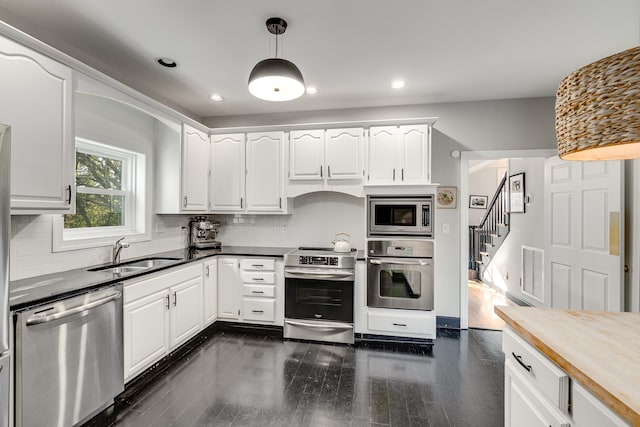 kitchen with white cabinets, stainless steel appliances, hanging light fixtures, and dark wood-type flooring