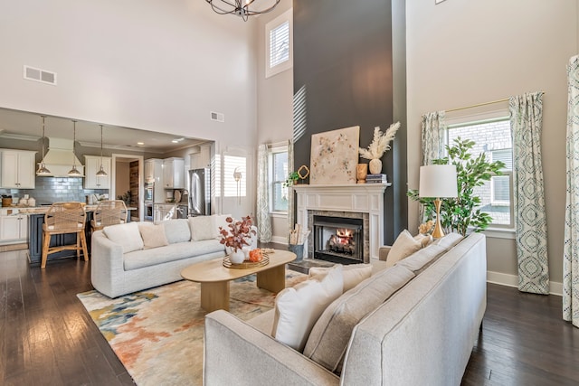 living room with a tile fireplace, dark hardwood / wood-style flooring, a towering ceiling, and a notable chandelier