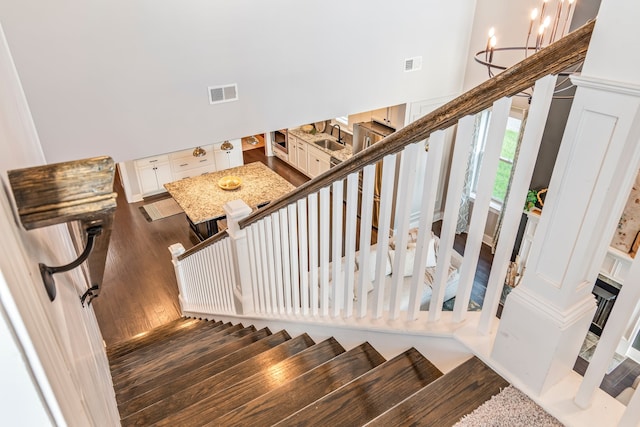 stairs featuring hardwood / wood-style floors, sink, a high ceiling, and a chandelier