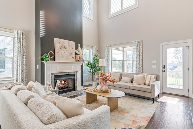 living room with a healthy amount of sunlight, wood-type flooring, a towering ceiling, and a tiled fireplace