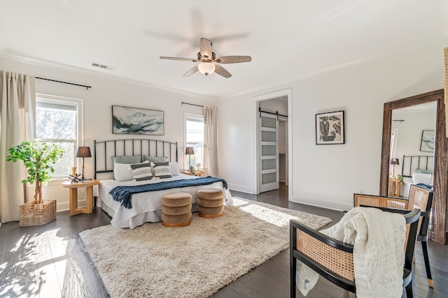 bedroom featuring a barn door, a walk in closet, ceiling fan, and dark hardwood / wood-style floors