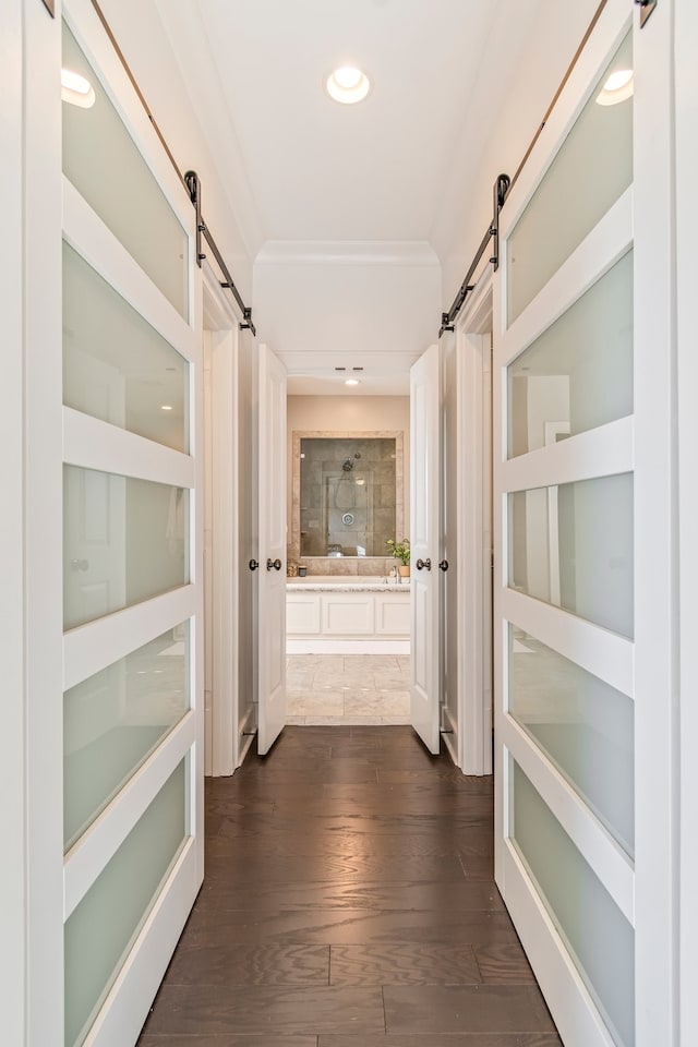 corridor featuring a barn door, crown molding, and dark hardwood / wood-style flooring