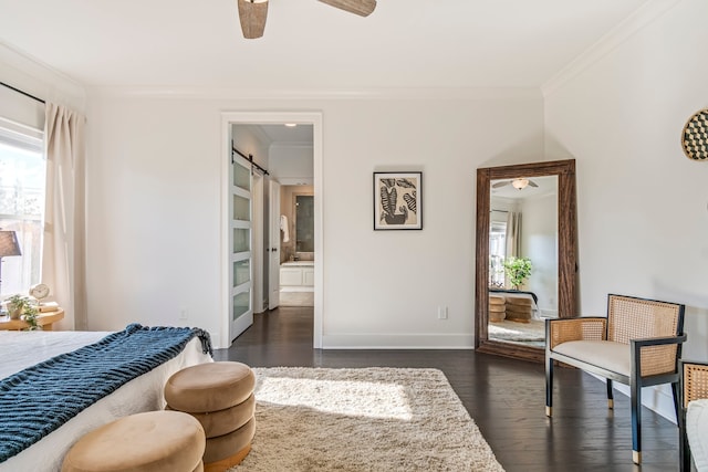 bedroom with ceiling fan, crown molding, dark wood-type flooring, a barn door, and connected bathroom