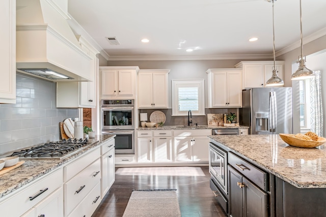 kitchen with white cabinets, ornamental molding, custom range hood, and appliances with stainless steel finishes