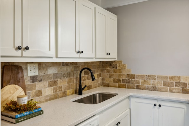 kitchen featuring white cabinets, backsplash, light stone countertops, and sink