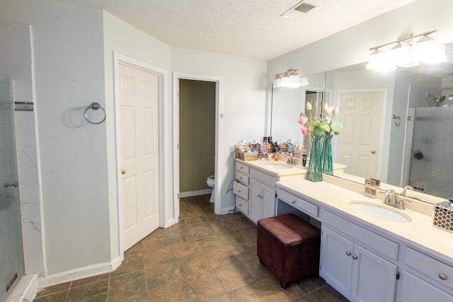 bathroom with toilet, vanity, a textured ceiling, and walk in shower