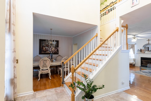 stairway with crown molding, wood-type flooring, and ceiling fan with notable chandelier