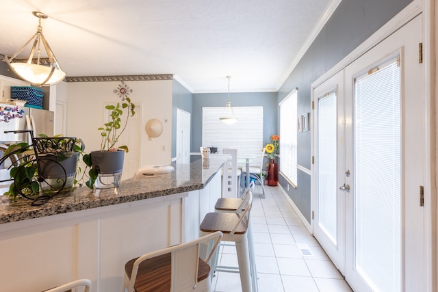 kitchen with dark stone countertops, stainless steel fridge, crown molding, decorative light fixtures, and light tile patterned floors