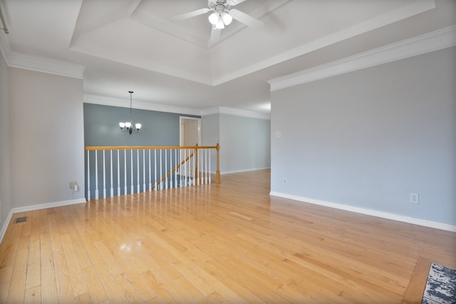 empty room with hardwood / wood-style flooring, ceiling fan with notable chandelier, ornamental molding, and a tray ceiling