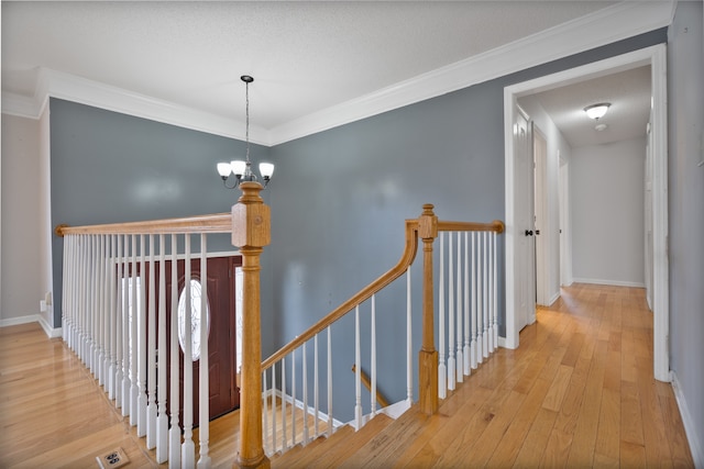 hallway with a notable chandelier, wood-type flooring, and ornamental molding