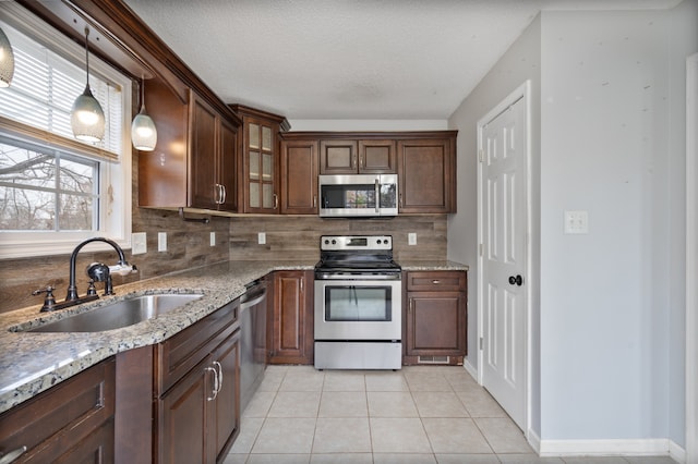 kitchen with sink, backsplash, decorative light fixtures, light tile patterned floors, and appliances with stainless steel finishes