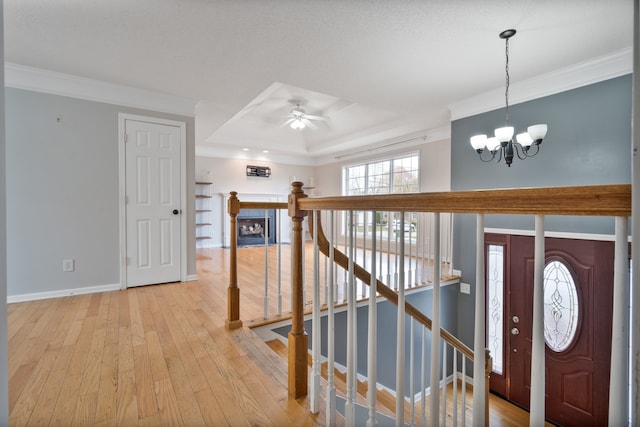 entryway featuring ceiling fan with notable chandelier, ornamental molding, a tray ceiling, and light hardwood / wood-style flooring