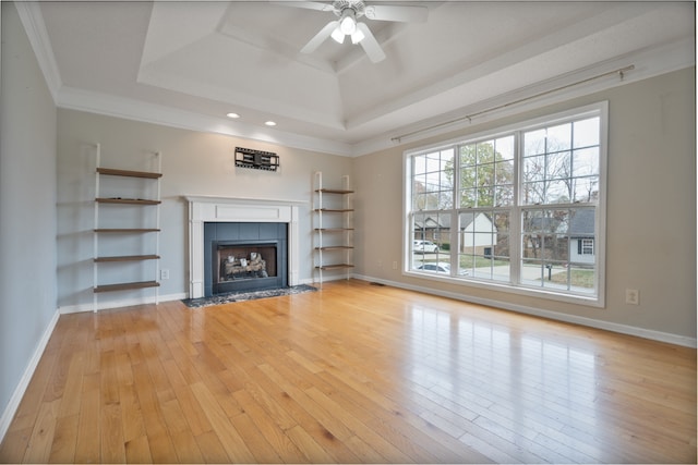 unfurnished living room featuring a tile fireplace, a raised ceiling, crown molding, ceiling fan, and light wood-type flooring