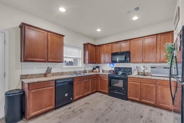 kitchen featuring decorative backsplash, light wood-type flooring, light stone counters, sink, and black appliances