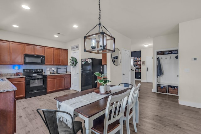 kitchen featuring black appliances, decorative backsplash, light wood-type flooring, light stone countertops, and decorative light fixtures