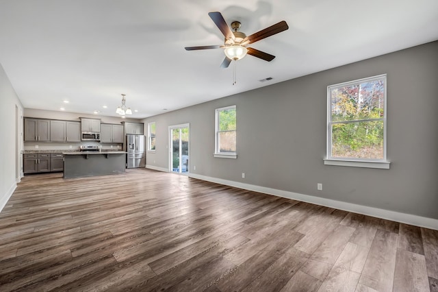 unfurnished living room with dark hardwood / wood-style floors and ceiling fan with notable chandelier