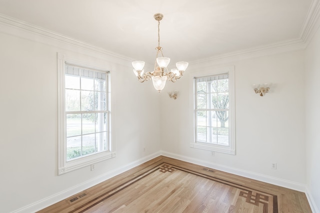 spare room with a wealth of natural light, ornamental molding, a notable chandelier, and hardwood / wood-style flooring