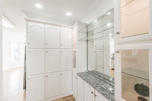 kitchen with white cabinetry, crown molding, dark stone counters, and light hardwood / wood-style flooring