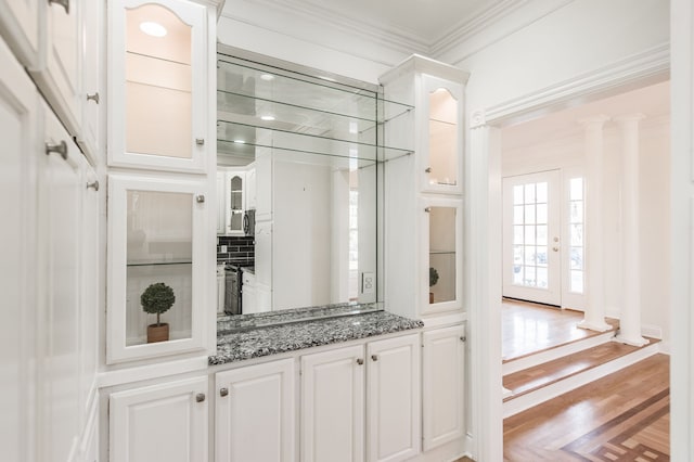 kitchen featuring white cabinets, crown molding, light hardwood / wood-style flooring, dark stone countertops, and decorative columns