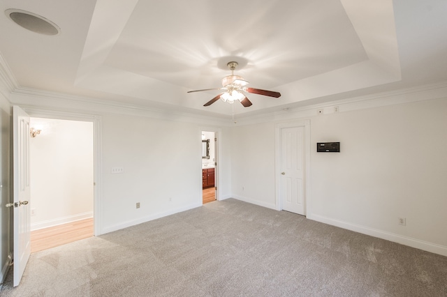 carpeted empty room with a raised ceiling, ceiling fan, and ornamental molding