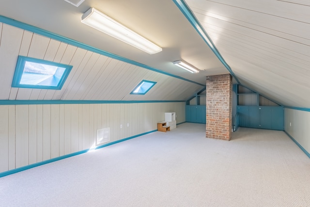 additional living space with carpet, lofted ceiling with skylight, and wooden walls