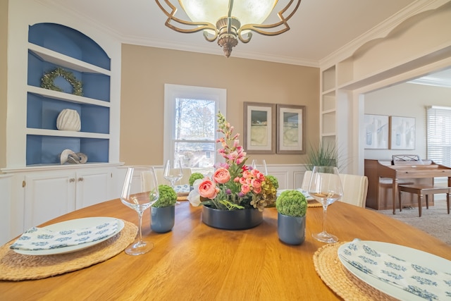 dining room featuring a chandelier, built in features, a healthy amount of sunlight, and ornamental molding