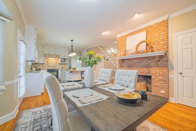 dining area with light hardwood / wood-style floors, ornamental molding, sink, and a brick fireplace