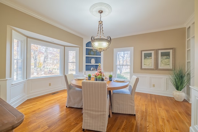 dining room with built in shelves, light hardwood / wood-style floors, a wealth of natural light, and ornamental molding