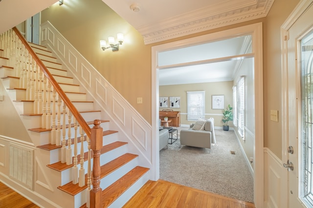 stairs with crown molding, plenty of natural light, and hardwood / wood-style flooring