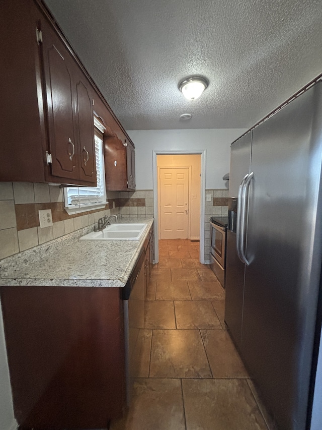 kitchen with dark brown cabinetry, sink, stainless steel appliances, tasteful backsplash, and a textured ceiling