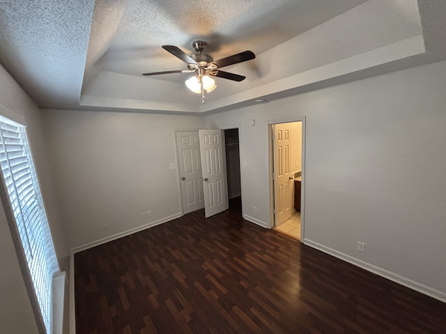 unfurnished bedroom featuring ensuite bath, ceiling fan, a raised ceiling, dark hardwood / wood-style flooring, and a textured ceiling