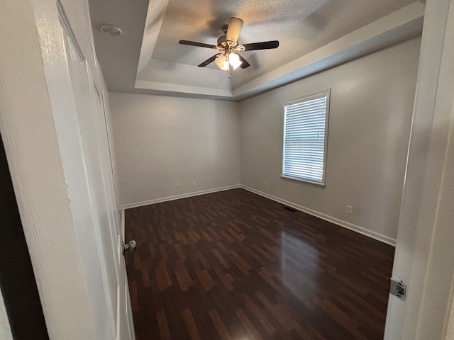 empty room with ceiling fan, a raised ceiling, and dark wood-type flooring