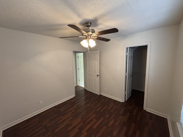 unfurnished bedroom featuring ceiling fan, dark wood-type flooring, a textured ceiling, a walk in closet, and a closet