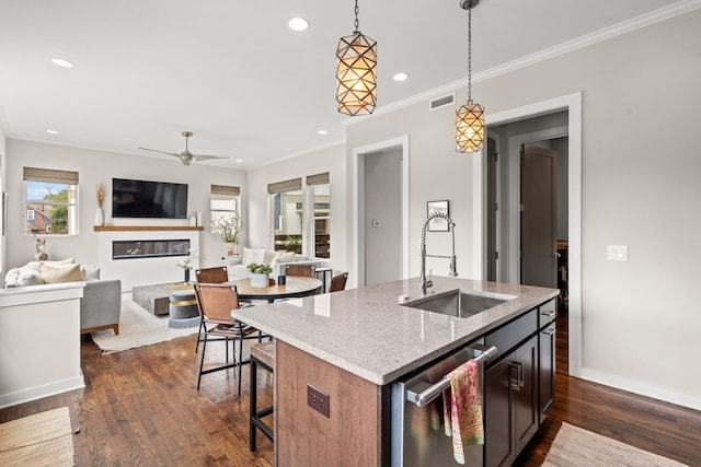 kitchen featuring sink, dark wood-type flooring, hanging light fixtures, light stone counters, and a kitchen island with sink